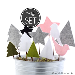 Può includere: Un set di 11 decorazioni per l'albero di Natale in feltro di vari colori e forme, tra cui verde, bianco, grigio, rosa e nero. Le decorazioni sono disposte in un secchio di metallo con muschio.