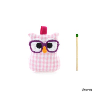 Puede incluir: Juguete de peluche de b&uacute;ho de guinga rosa y blanco con gafas moradas y pico naranja.