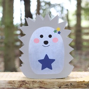 May include: A gray hedgehog-shaped cutout with a light blue belly, a dark blue star on the center, pink cheeks, black eyes and nose, and three small stars in yellow, green, and blue near the top. The text KerstinBremer.de is visible at the bottom.