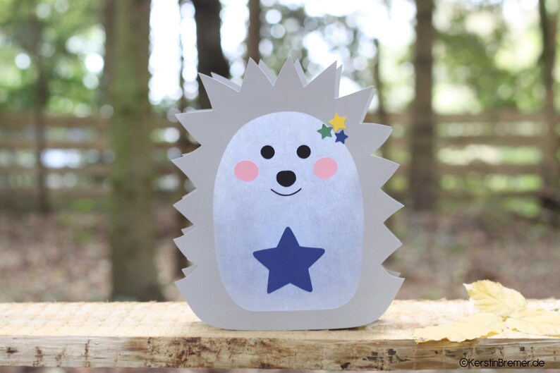 May include: A gray hedgehog-shaped cutout with a light blue belly, a dark blue star on the center, pink cheeks, black eyes and nose, and three small stars in yellow, green, and blue near the top. The text KerstinBremer.de is visible at the bottom.
