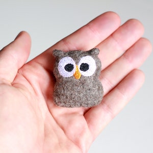 May include: A small brown felt owl with embroidered white eyes and an orange beak.