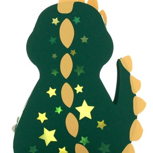 Pode incluir: Uma lanterna de papel verde em forma de dinossauro com uma espinha dorsal amarela e estrelas. A lanterna &eacute; decorada com estrelas amarelas e verdes.