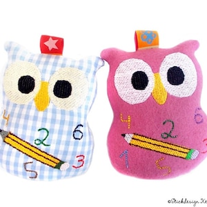 Puede incluir: Dos juguetes de peluche con forma de búho. Uno es de cuadros vichy azul claro con números bordados y un lápiz amarillo. El otro es rosa con números bordados y un lápiz amarillo. Ambos tienen ojos negros grandes, picos amarillos y un pequeño lazo en la parte superior.