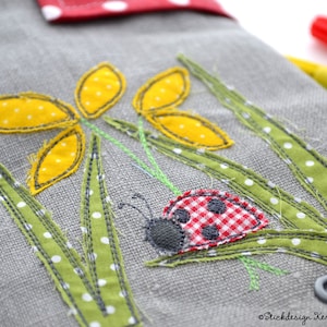 May include: A grey fabric pencil case with a ladybug, yellow flowers, and green grass embroidered on it. The fabric has white polka dots.