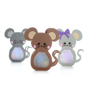 May include: Three mouse-shaped decorative figures standing in a row. The centre figure is brown, while the two outer figures are grey. Each mouse features a clear, iridescent belly, pink cheeks, black whiskers, and a curved tail. One grey mouse wears a purple bow.