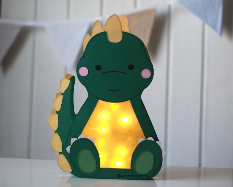 Fertig gebastelte Dinosaurier Stegosaurus Kinderlaterne aus grünem Tonkarton, die im Dunkeln leuchtet. Bastelvorlage für St. Martin