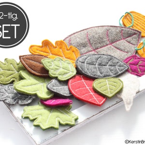 May include: A set of 22 felt leaf shapes in various colours and sizes, including green, red, orange, brown, grey, and pink. The leaves have white stitching around the edges. The set is labelled "22-tlg. SET".