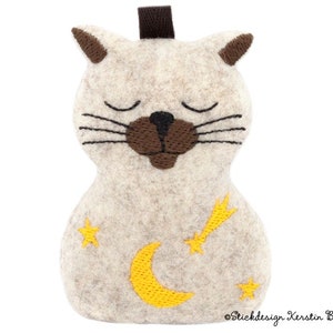 Könnte beinhalten: Eine beige Filzkatze mit gestickten braunen Augen, einer schwarzen Nase und einem gelben Halbmond- und Sternschnuppen-Design. Die Katze schläft mit geschlossenen Augen.