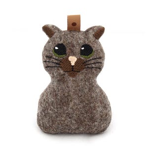 May include: A brown felt cat toy with embroidered eyes, nose and whiskers. The cat is sitting upright with a loop on the top of its head.