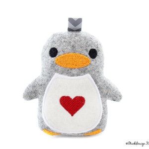 May include: A grey felt penguin plush toy with a white felt belly and a red embroidered heart. The penguin has a black embroidered beak and eyes.