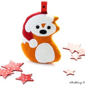 May include: A plush orange fox wearing a red Santa hat with white trim. The fox is surrounded by red wooden stars with white polka dots.