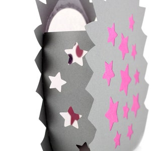 May include: A gray paper lantern with jagged, spiked edges featuring cut-out star shapes and applied pink star decals. The structure is curved, revealing a white interior surface. The text KerstinBremer.de is printed at the bottom left.