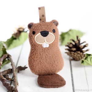 May include: A brown plush beaver toy with a black nose and white teeth. The beaver has a brown tail and is hanging from a brown and white polka dot ribbon.
