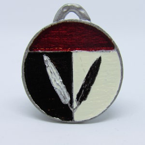 May include: A round pendant with a silver-colored loop. The pendant is divided into four sections: a red top, a black left side, and a white right side, with two black and white feather-like shapes.