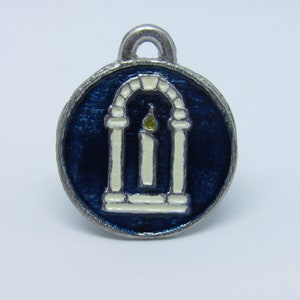 May include: A silver charm with a blue enamel background and a white enamel candle in an archway.