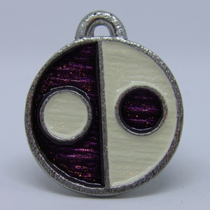 May include: A silver charm with a yin yang design. One half is purple with a white circle in the center, and the other half is white with a purple circle in the center.