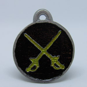 May include: A silver charm with a black background and two crossed swords in yellow enamel.