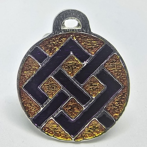 May include: A round silver pendant with a purple and gold design. The design is a geometric pattern of interlocking squares and lines.