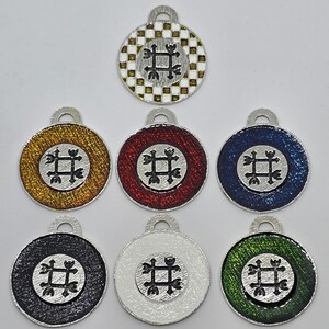 May include: Set of seven round metal charms with a black and white symbol in the center. The charms are in different colors: gold, red, blue, black, white, and green. The charms have a checkered pattern on the back.