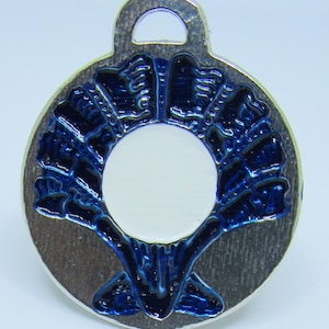 May include: A silver charm with a blue enamel design. The charm features a stylized image of a tree with a white circle in the center. The charm has a loop at the top for attaching to a bracelet or necklace.