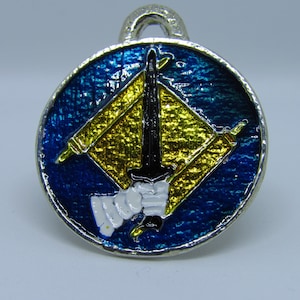 May include: A silver charm with a blue enamel background and a yellow diamond shape with a black sword in the center. The sword is surrounded by two white scrolls.