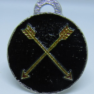May include: A black metal charm with a silver loop. The charm features two gold arrows with red tips, crossed over each other.