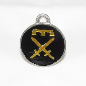 May include: A round, silver charm with a black enamel background. The charm features a gold-colored design of two crossed swords with a stylized 'M' above them.