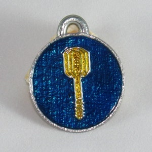 May include: A silver charm with a blue enamel background and a gold key design.