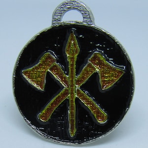 May include: A silver pendant with a black background and a gold design of two crossed axes and a spear. The pendant has a loop at the top for attaching to a chain.