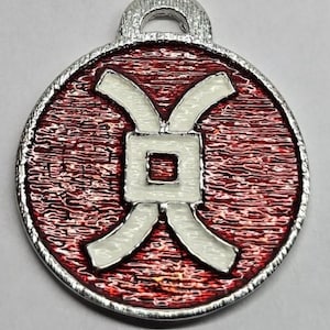 May include: A round pendant with a silver-colored loop at the top. The pendant has a textured red background with a white geometric design in the center. The outer edge is silver-colored.