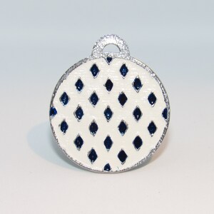 May include: A white oval ornament with a silver rim and a blue diamond pattern.