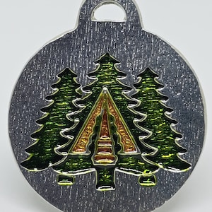 May include: A silver round charm with a green, orange, and yellow enamel design of three pine trees with a tent in the center.