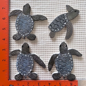 May include: Four ceramic sea turtle tiles in shades of gray with white accents. The turtles are in various poses, with some facing forward and others facing sideways. The tiles are approximately 4 inches in size.
