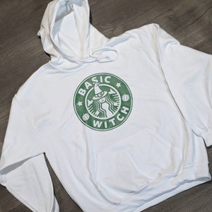 May include: White hoodie with a green graphic of a witch with a pumpkin and the text "BASIC WITCH" in a circle.