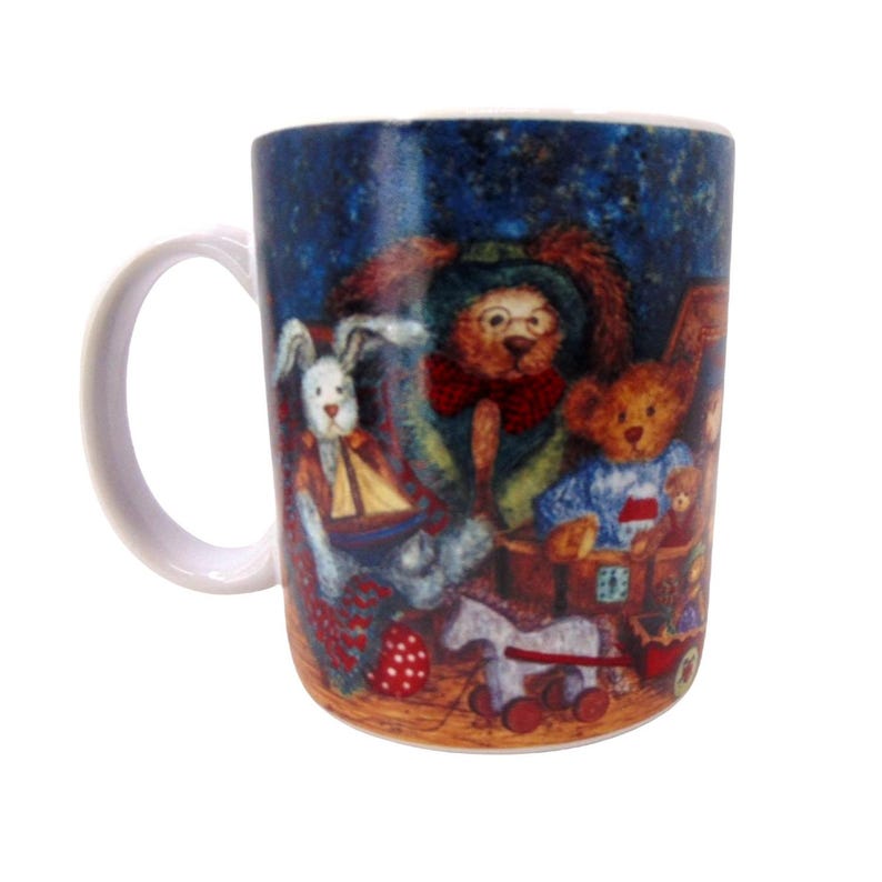 May include: A white ceramic mug featuring a colorful illustration of various stuffed animals, including a rabbit holding a toy boat, a bear wearing glasses and a red bow tie, and another bear in a blue sweater, all set against a dark blue background.