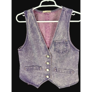 May include: A vintage purple denim vest with a button-up front, two front pockets, and a V-neck. The vest is hanging on a white hanger against a black background. The vest has a faded, acid-wash appearance.