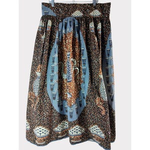 Op de afbeelding: Een lange, bedrukte rok met een bruin, blauw en wit ontwerp. De rok heeft een elastische tailleband en een volle, vloeiende silhouet. De stof heeft een herhalend patroon van vazen, kommen en andere decoratieve elementen.