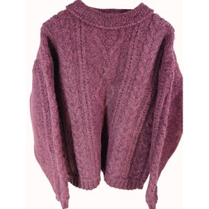 Puede incluir: Un suéter de punto trenzado de color malva con cuello redondo. El suéter tiene un patrón texturizado y mangas largas. La prenda está hecha de un material grueso y cálido, perfecto para climas más fríos.