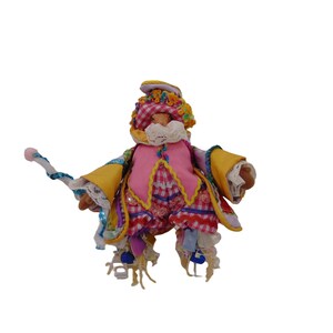 May include: A whimsical doll with a pink vest, yellow sleeves, and a checkered head covering. The doll has a white beard and holds a decorative staff. The doll's outfit is adorned with lace, ribbons, and colorful embellishments.