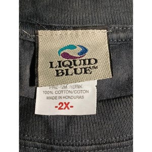 May include: Close-up of a gray t-shirt tag with the Liquid Blue logo in teal and blue. The tag also includes text that reads "100% Cotton/Coton Made in Honduras" and a size indicator of "-2X-".