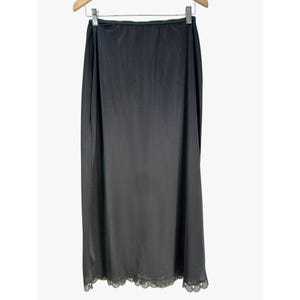 May include: A solid black full-length slip skirt featuring a smooth, lightweight fabric construction with a straight silhouette and a delicate, scalloped lace trim detail along the bottom hemline, suspended from a wooden clothes hanger.