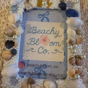 May include: A rectangular photo frame decorated with seashells, pearls, and snowflake accents. The frame has the words "Oh Boy" in gold letters and the text "Beachy Bloom Co." in the center. The frame is white and blue.