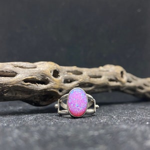 May include: A silver ring with a pink opal gemstone. The ring has a unique open design with two bands that cross over each other.
