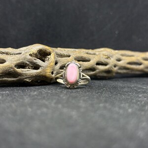May include: A silver ring with a pink oval gemstone set in a silver bezel. The ring has a delicate design with intricate details.