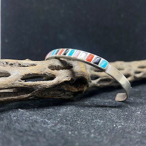 May include: A silver bracelet with a band of inlaid turquoise, red, black, and white stones.