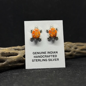 May include: A pair of sterling silver earrings featuring a turtle design with orange and red inlay. The earrings are displayed on a white card with the text "GENUINE INDIAN HANDCRAFTED STERLING SILVER".