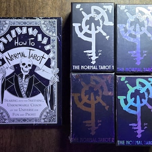 Könnte beinhalten: Ein schwarz-weiß illustriertes Buch mit dem Titel "How To Normal Tarot" und dem Text "Staring into the seething, unknowable chaos of the universe for fun and profit". Drei schwarze Boxen mit holografischen Designs und dem Text "The Normal Tarot" sind übereinander gestapelt.