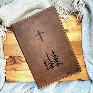 May include: A brown leather journal with a cross and three trees engraved on the front. The journal has the text "Matthew 5:16" on the bottom right corner.