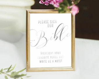 May include: A gold-framed sign with the text "Please sign our Bible. Highlight your favorite verse and write us a note!" in silver lettering.
