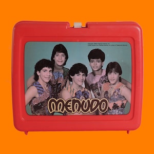 May include: A vintage red plastic lunchbox featuring a color image of the pop group Menudo. The lunchbox has a white latch and a picture of the band members. The word "Menudo" is printed in a stylized font.